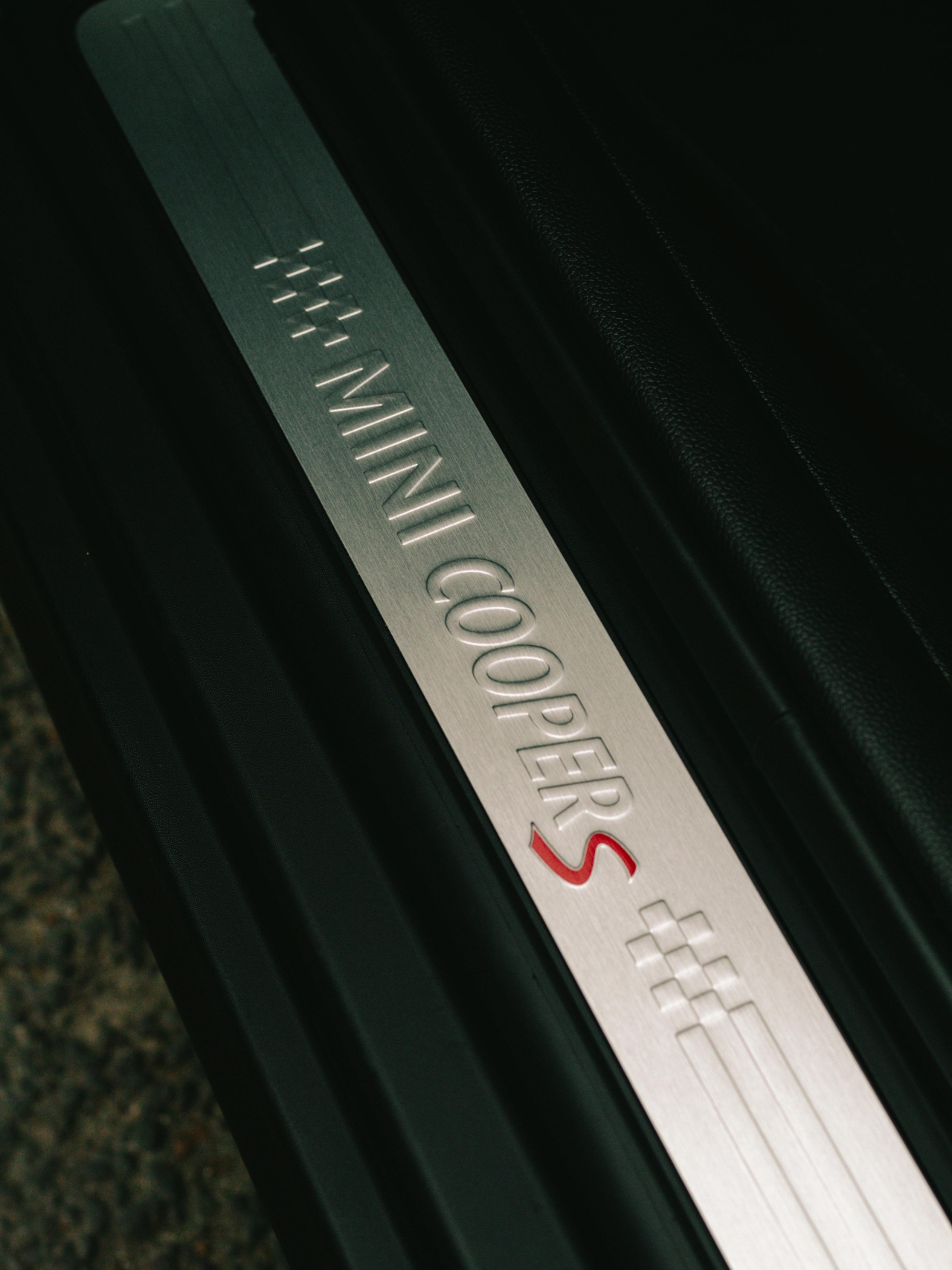 Oryginalne detale i części wnętrza z demontażu dla Twojego MINI Cooper S Zbliżenie na aluminiową listwę progową z tłoczonym logo MINI Cooper S we wnętrzu samochodu, symbolizującą sportowy charakter pojazdu.